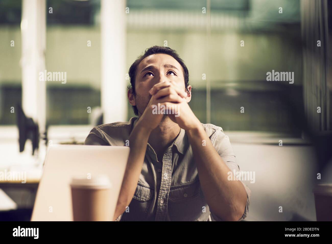 Junger asiatischer Geschäftsleute, der am Schreibtisch im Büro sitzt und nachdenkt Stockfoto