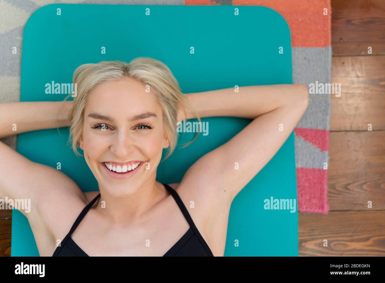 Blonde lächelnde Frau liegt auf dem Rücken auf Yoga-Matte Stockfoto