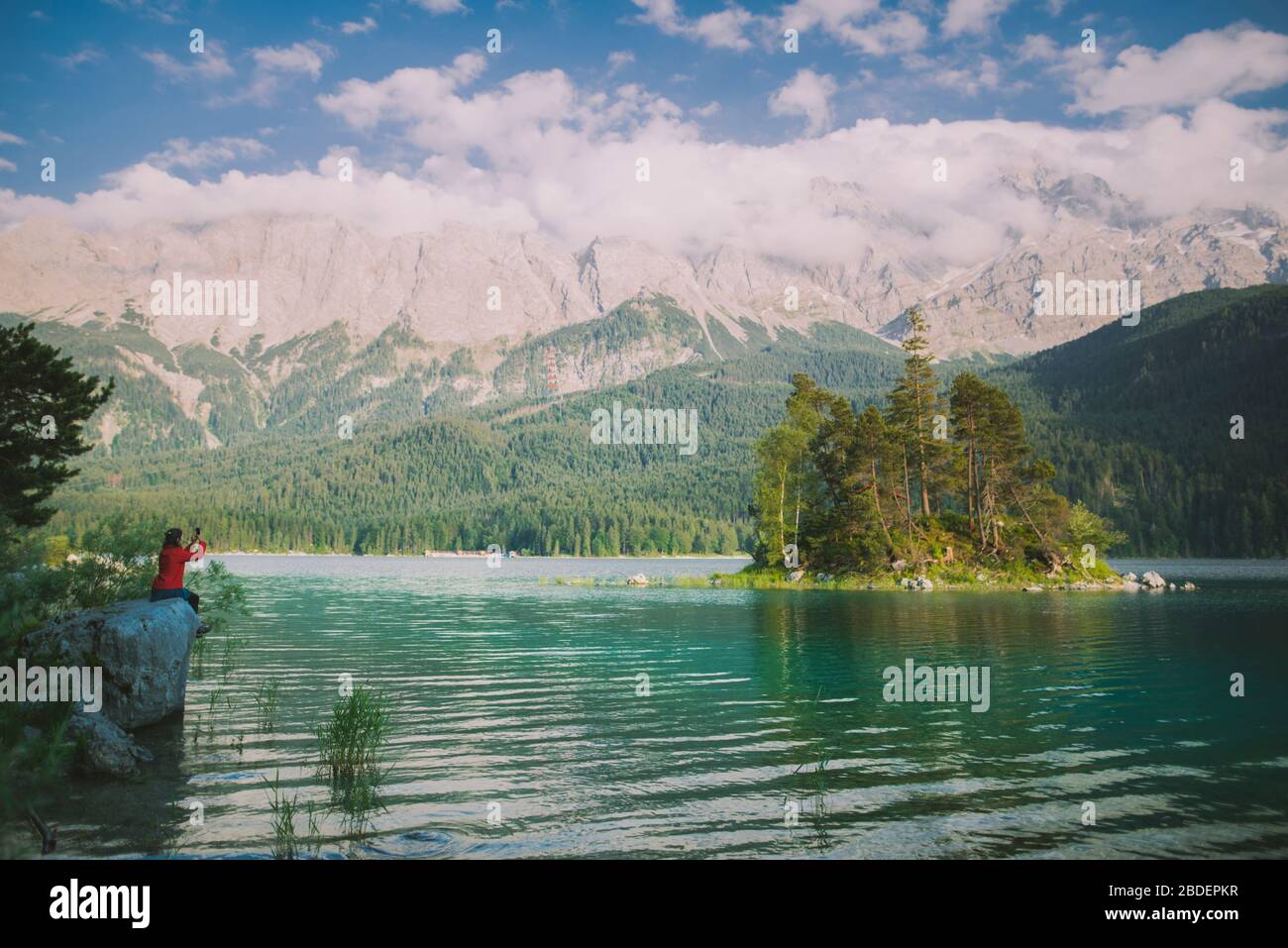 Deutschland, Bayern, Eibsee, Junge Frau sitzt auf Felsen am Eibsee in den bayerischen Alpen und fotografiert Landschaft mit Smartphone Stockfoto