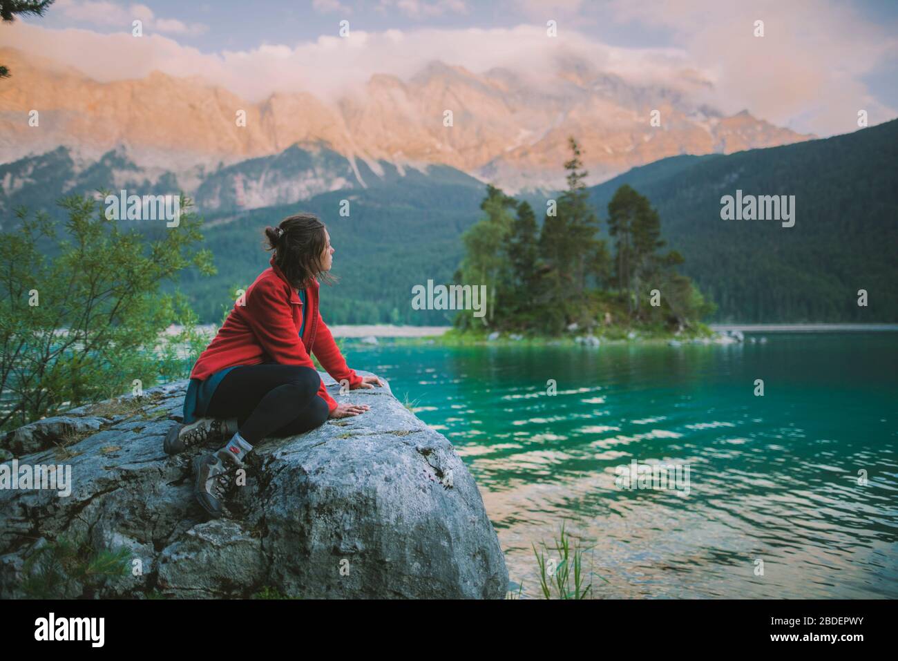 Deutschland, Bayern, Eibsee, Junge Frau auf Felsen sitzend und mit Blick auf den malerischen Blick am Eibsee in den bayerischen Alpen Stockfoto