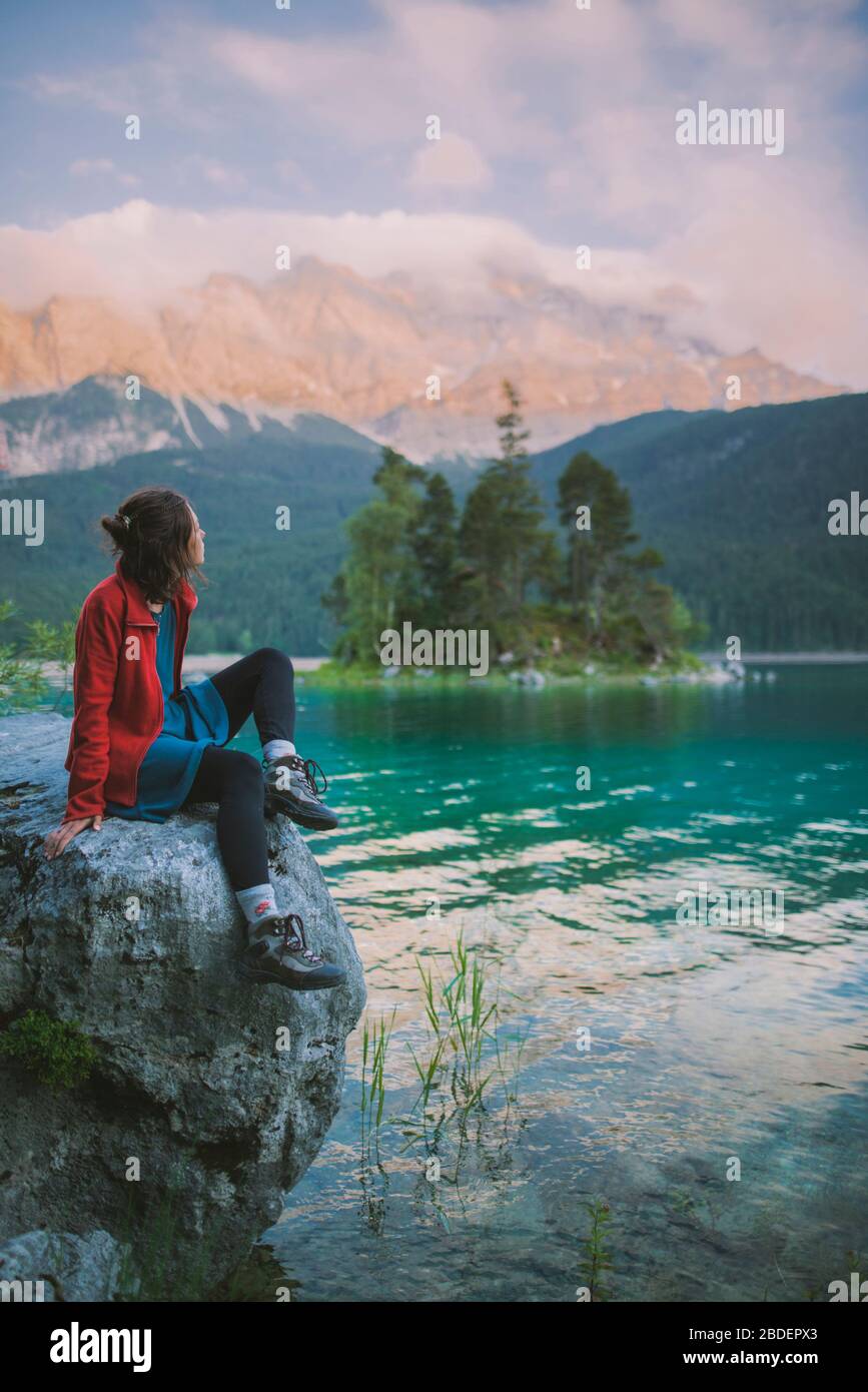 Deutschland, Bayern, Eibsee, Junge Frau auf Felsen sitzend und Blick auf den malerischen byÂ EibseeÂ See in den bayerischen Alpen Stockfoto