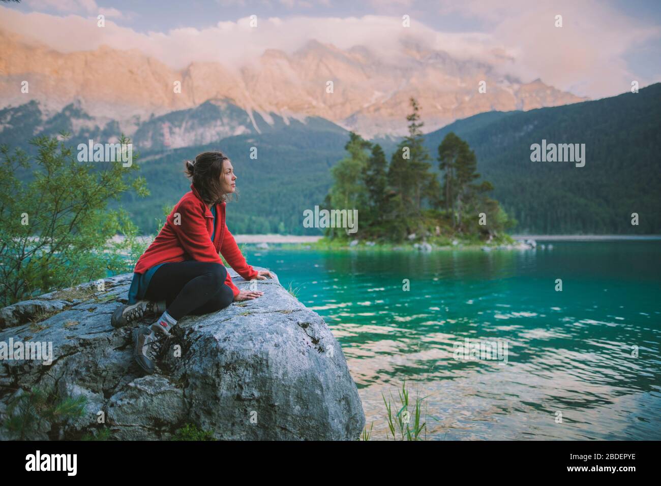 Deutschland, Bayern, Eibsee, Junge Frau auf Felsen sitzend und mit Blick auf den malerischen Blick am EibseeÂ See in den bayerischen Alpen Stockfoto