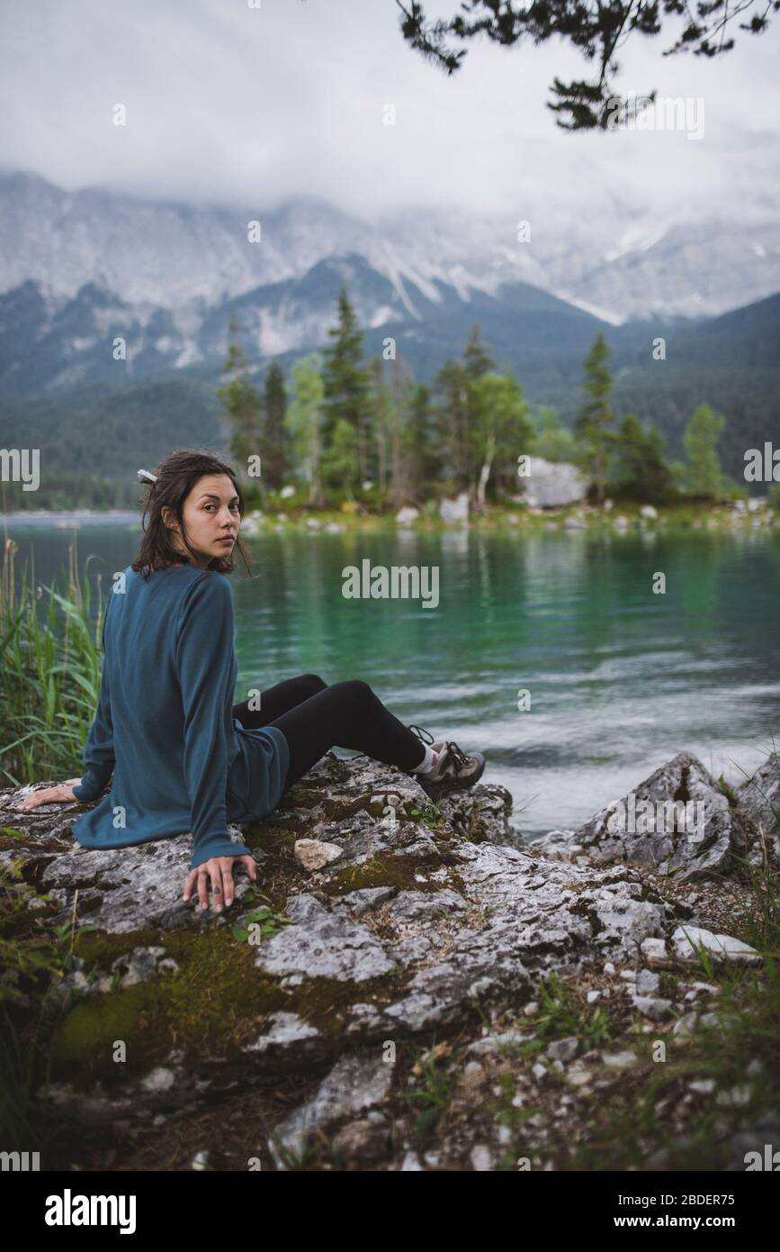 Deutschland, Bayern, Eibsee, Portrait einer jungen Frau, die am Ufer des Eibsees in den bayerischen Alpen auf Felsen sitzt Stockfoto