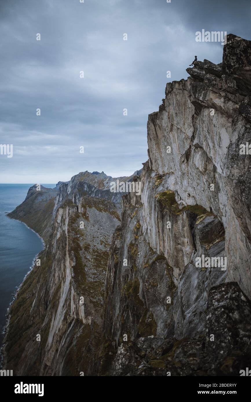 Norwegen, Senja, Mann sitzt am Rande einer steilen Klippe auf dem Gipfel ofÂ SeglaÂ Berg Stockfoto