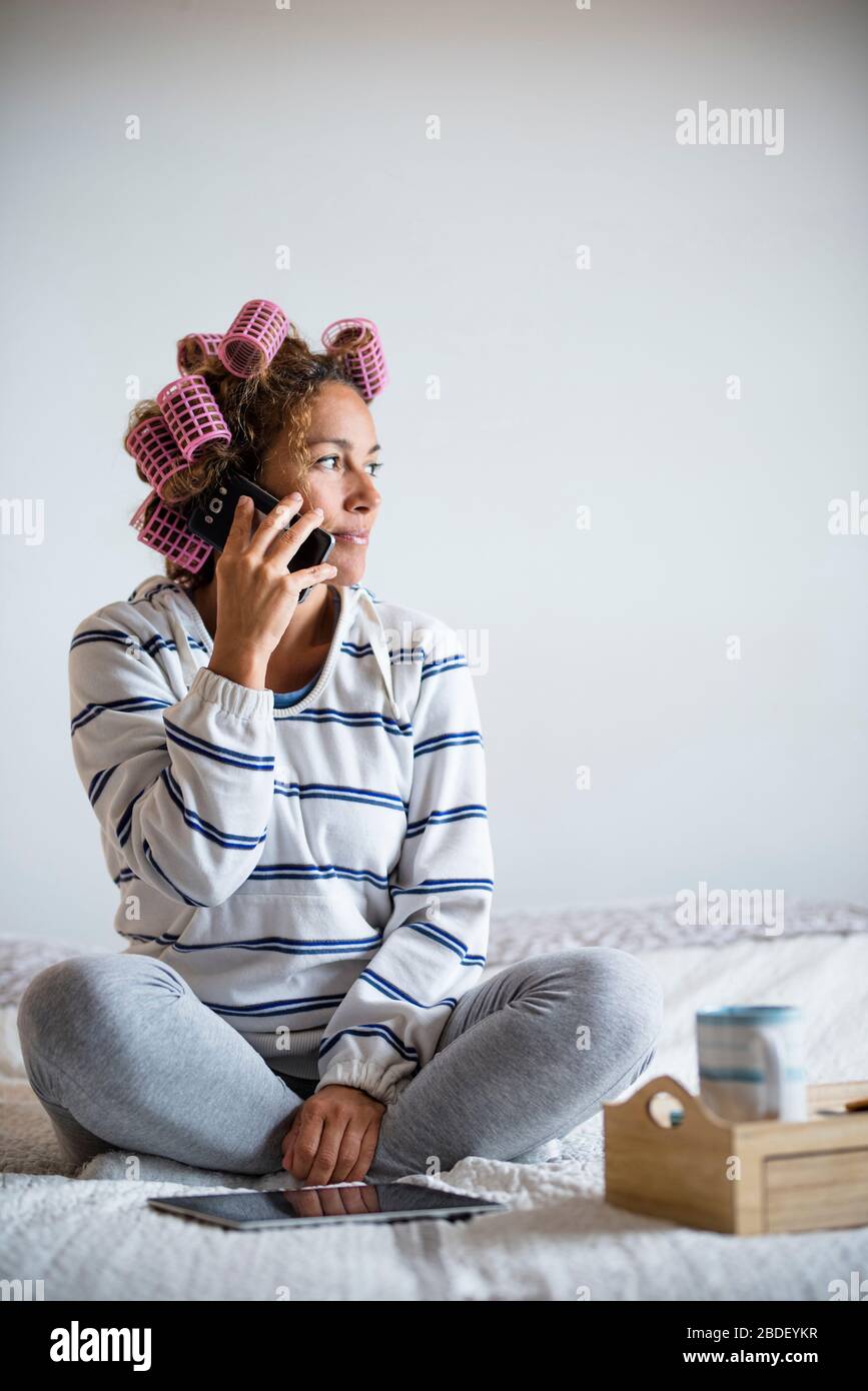 Frau mit hairÂ curlersÂ sitzt auf dem Bett und spricht auf dem Handy Stockfoto