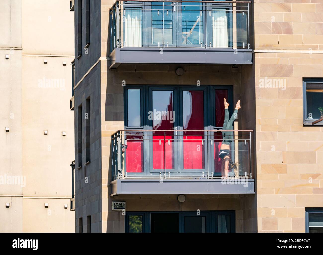 Leith, Edinburgh, Schottland, Großbritannien. April 2020. Covid-19 Lockdown: An einem der wärmsten Sonnentage in diesem Jahr mit Menschen in Lockdown. Eine Frau übt akrobatische Handstände auf einem Balkon in der Sonne Stockfoto