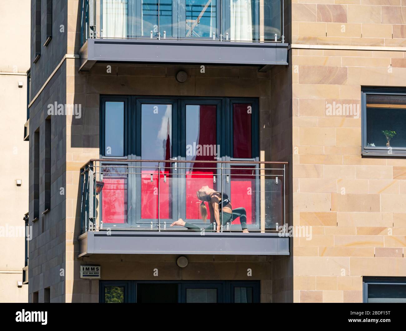 Leith, Edinburgh, Schottland, Großbritannien. April 2020. Covid-19 Lockdown: An einem der wärmsten Sonnentage in diesem Jahr mit Menschen in Lockdown. Eine Frau übt Akrobatik und Dehnungsübungen auf einem Balkon in der Sonne Stockfoto