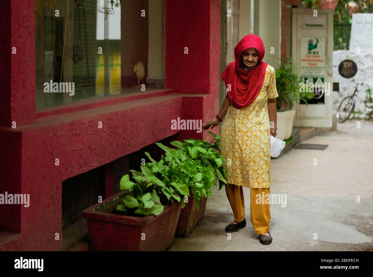 Ältere Frau mit nachdenklicher Ausdrucksweise, die vor dem Laden in der Straße in Delhi, Indien, bunte, traditionelle indische Kleidung trägt. Stockfoto