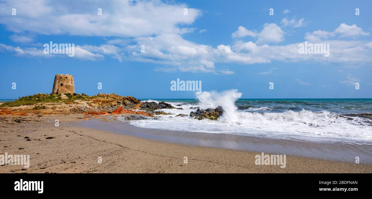 Das Wahrzeichen der Stadt Bari Sardo, der Torre di Barì, ein Turm, der auf einem Felsvorsprung am Strand mit beigem Sand und Meer mit schäumenden Wasser erbaut wurde Stockfoto