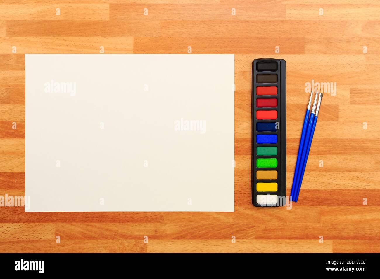 Mit Blick auf eine Palette farbiger Farben, Bürsten und einem weißen Blatt auf einem Holzhintergrund Stockfoto