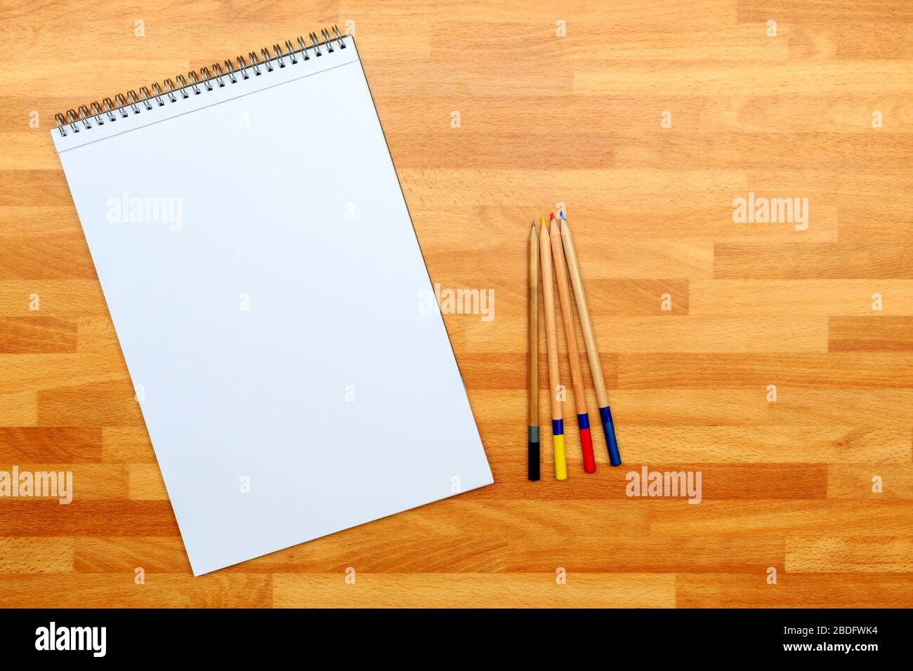 Blick nach unten auf ein angewinkelt weißes Zeichenpolster und farbige Bleistifte auf einem Holzhintergrund Stockfoto