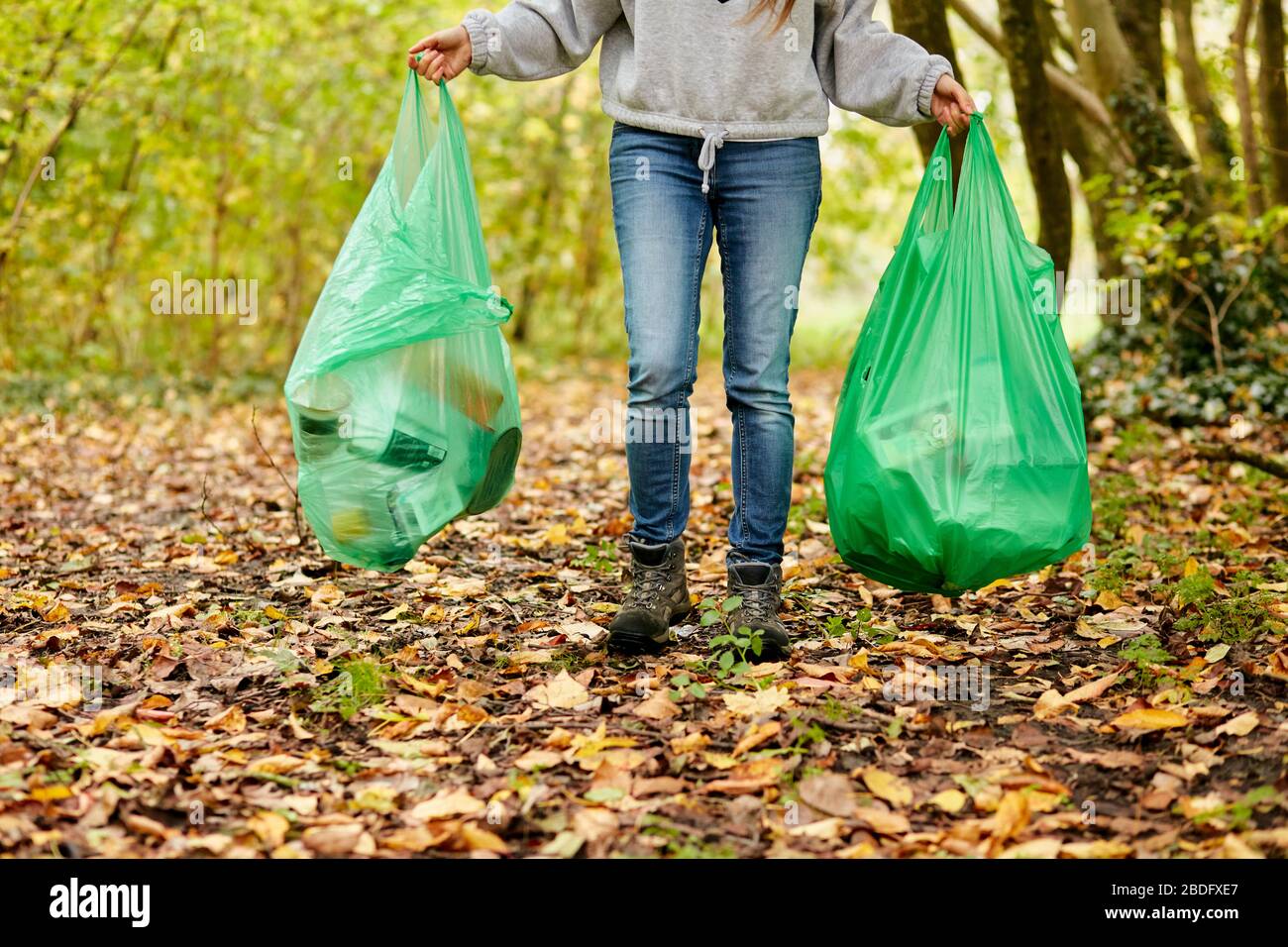 Frau, die im Wald spazieren geht und zwei Plastiktüten voller Müll hält Stockfoto