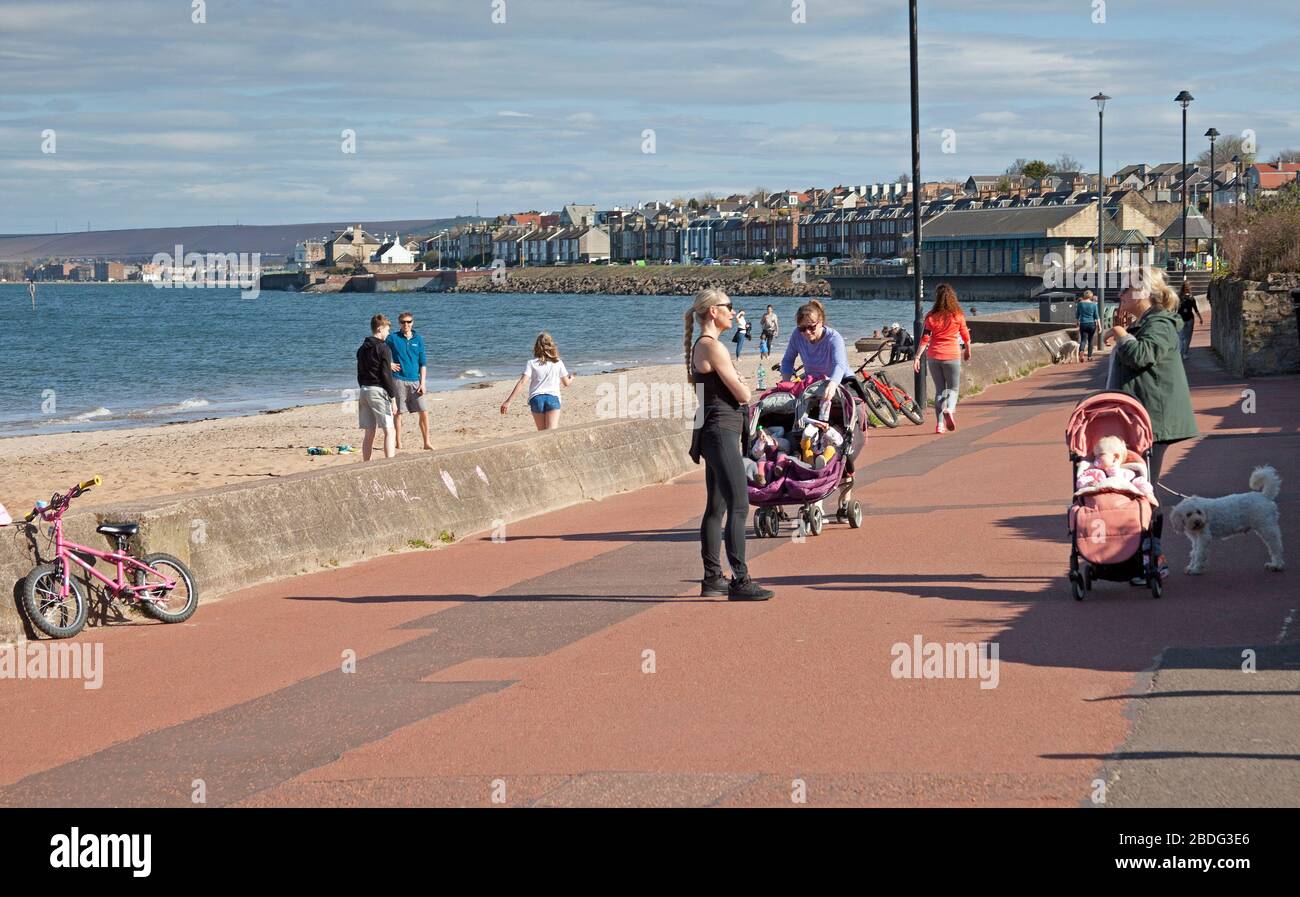 Portobello Beach, Edinburgh, Schottland, Großbritannien. April 2020. 18 Grad und voller Sonnenschein brachten Sonnenanbeter ans Meer, die meisten sozialen Distanzierungen, aber nicht die Menschenmassen, die erwartet würden, wenn es nicht den Coronavirus Lockdown gäbe und die Menschen hauptsächlich spazieren oder sitzen, anstatt auf dem Sand zu liegen. Ein männlicher und weiblicher Polizist auf der Promenade für einen Routinepassgang. Credit: Arch White/Alamy Live News Stockfoto