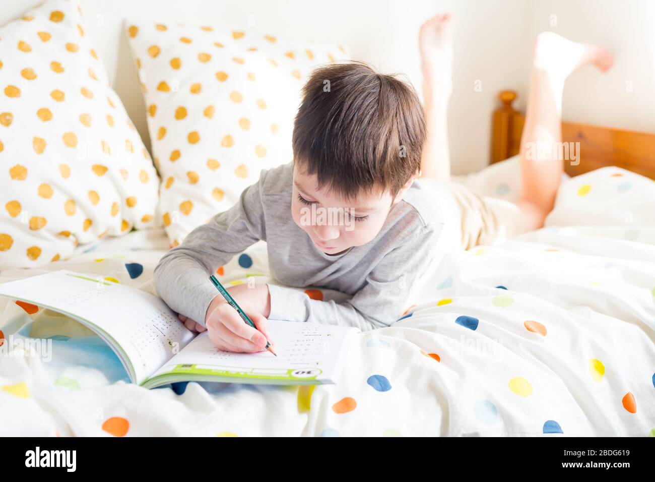 Online-Fernunterricht. Schuljunge im Bett und Hausaufgaben zu Hause machen, in Notizbuch schreiben. Quarantäne. Das Konzept, zu Hause zu bleiben Stockfoto