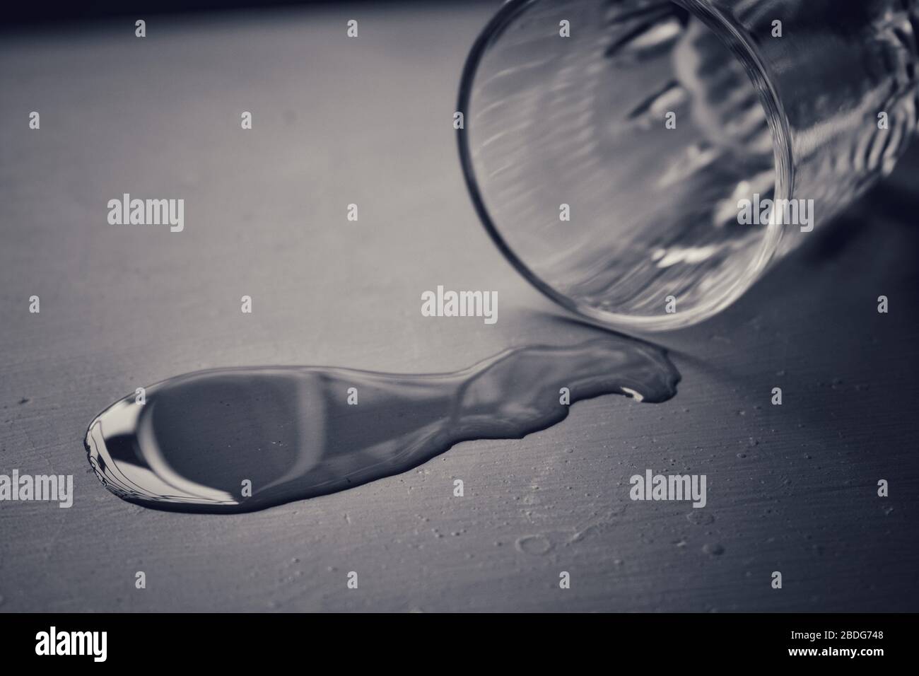 Schwarz-weißes Bild, in dem aus einem leeren Glas eine kleine Menge Wasser auf den Boden gegossen wird Stockfoto