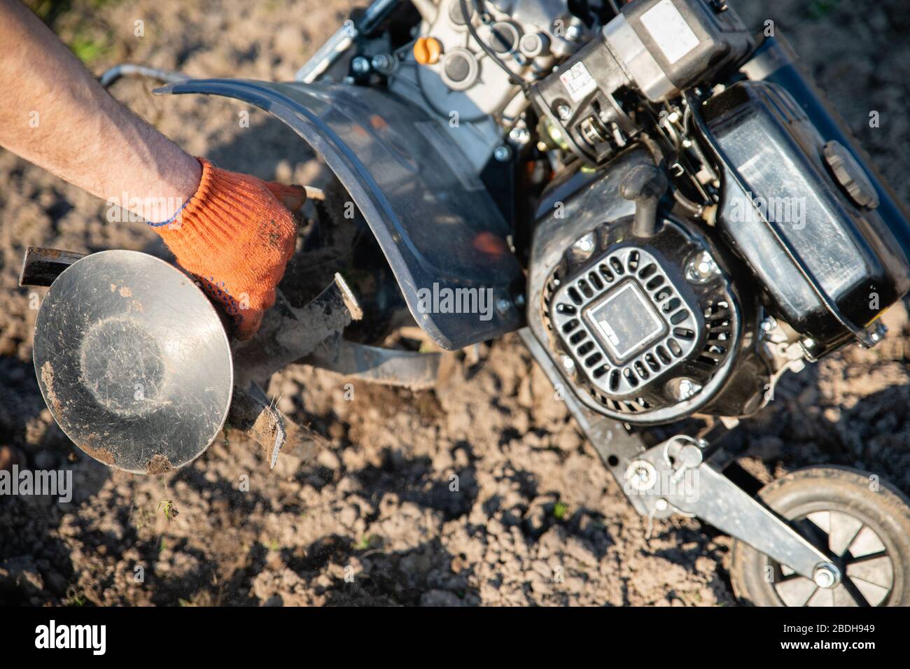 Kleine orange Pflügemaschine in den Händen eines Landwirts, der in schwarzem Boden anbaubar macht Stockfoto