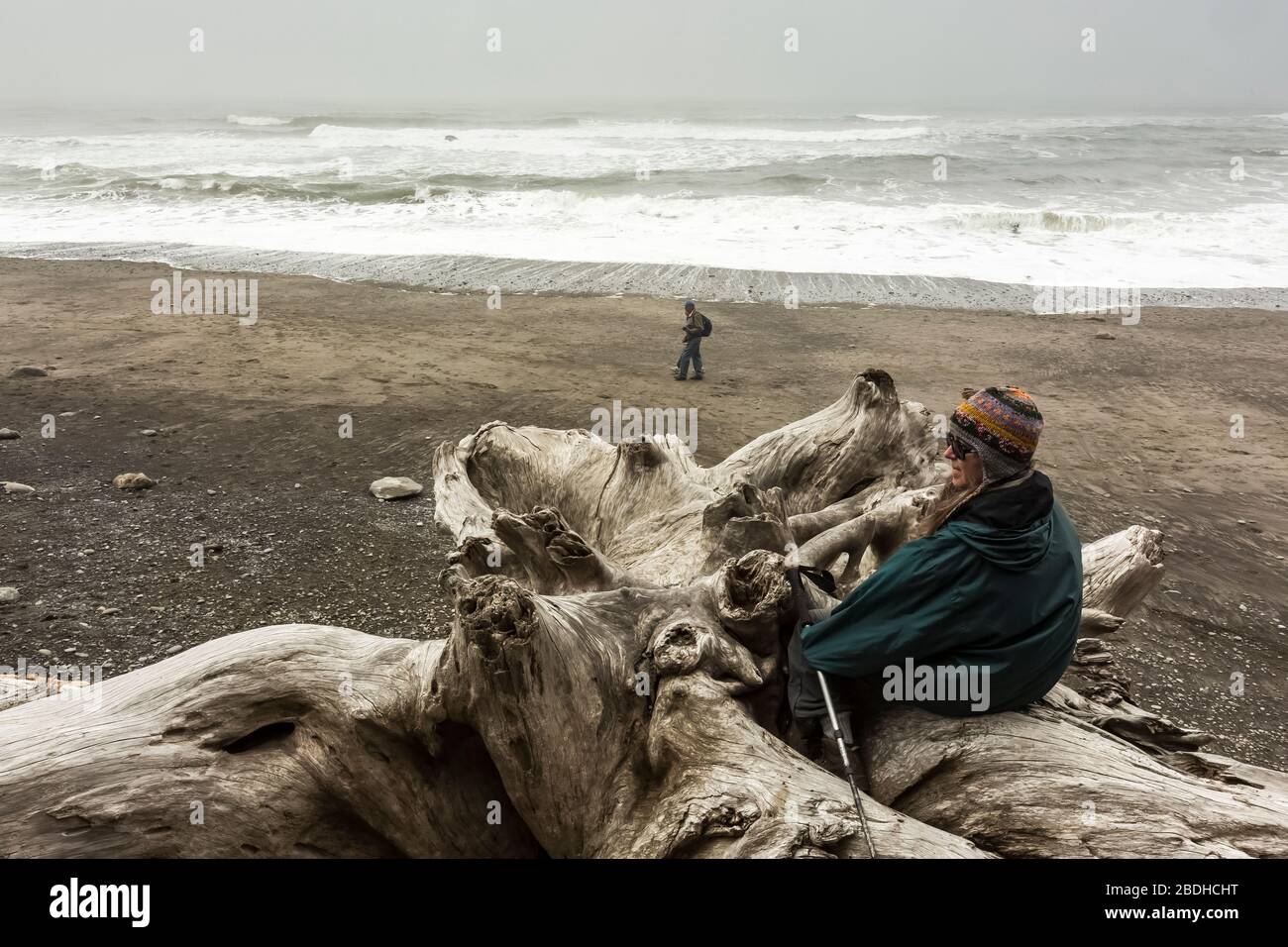 Karen Rentz ist an einem grauen Junitag mit Treibholz am Rialto Beach im Olympic National Park, Washington State, USA, mit dem Rucksack unterwegs Stockfoto