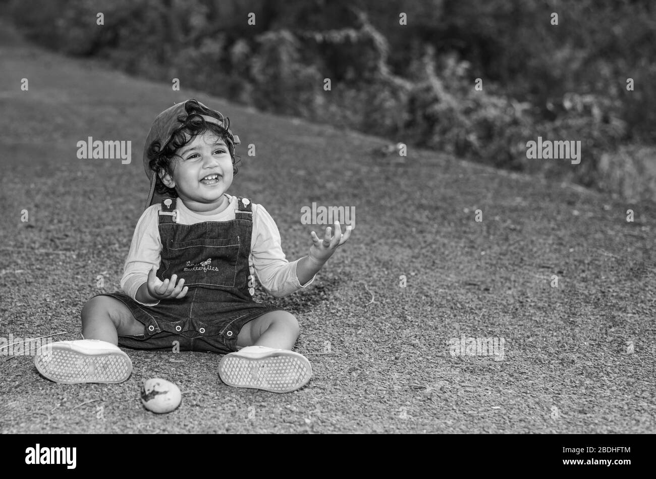 Margao, Goa/Indien - 2. April 2020 : spielerisch hübsches indisches Mädchen Kind/Kleinkind, das eine Mütze trägt, ein Buch liest und mit Feldern und Sonnenuntergang im Hintergrund spielt Stockfoto