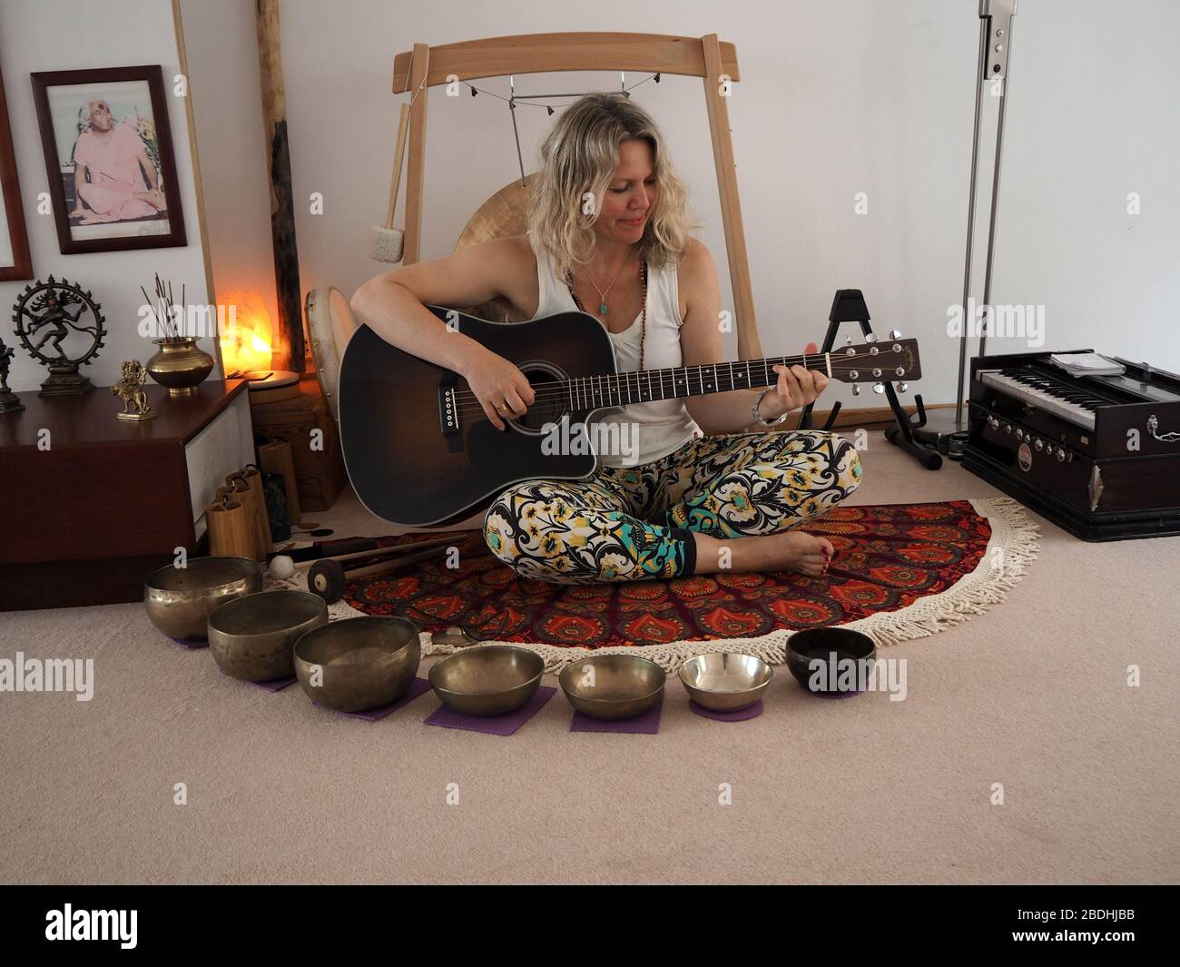 Junge Frau mit Gitarre, umgeben von Instrumenten für eine Klangheilung Stockfoto