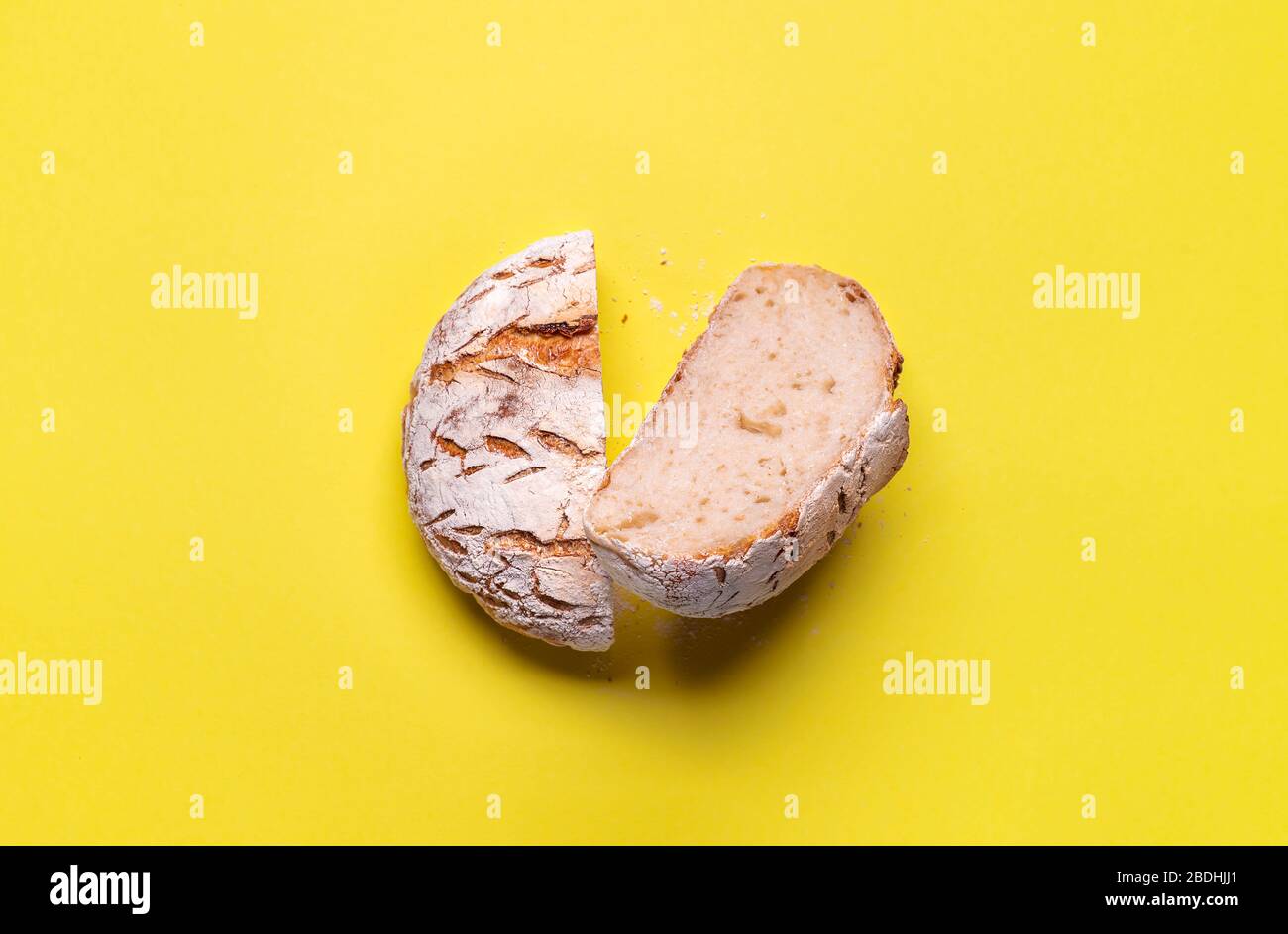 Handwerkliches Sauerteig Brot in Hälften geschnitten auf einem gelb-nahtlosen Hintergrund. Flat Lay aus hausgemachtem Weizenbrot ohne Hefe. Brot mit Allzweckmehl. Stockfoto