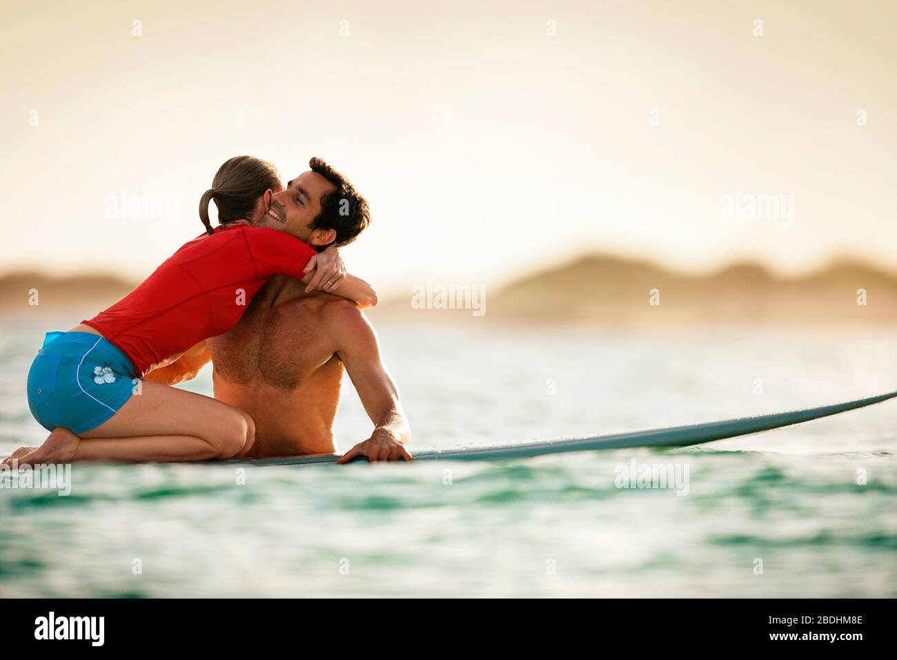 Frau kniet an einem Surfbrett und umarmte ihren Freund. Stockfoto