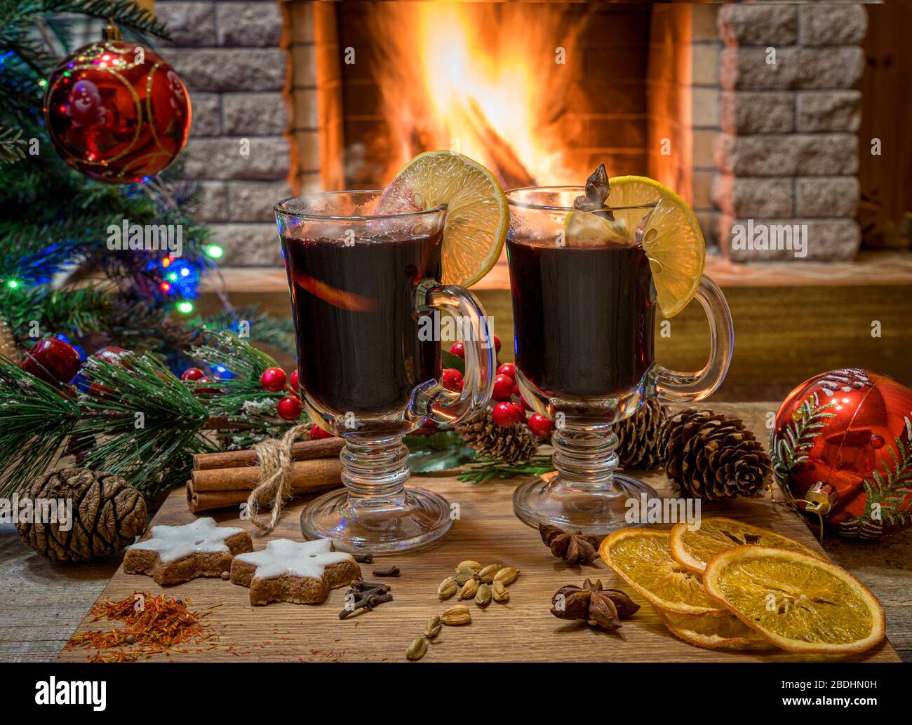 Gemütliche Weihnachts-Szene mit zwei Gläsern Glühwein auf einem Holzbrett vor Weihnachtsbaum dekorierte Spielzeuge und weihnachtslichter gegenüber dem brennenden Feuer Stockfoto