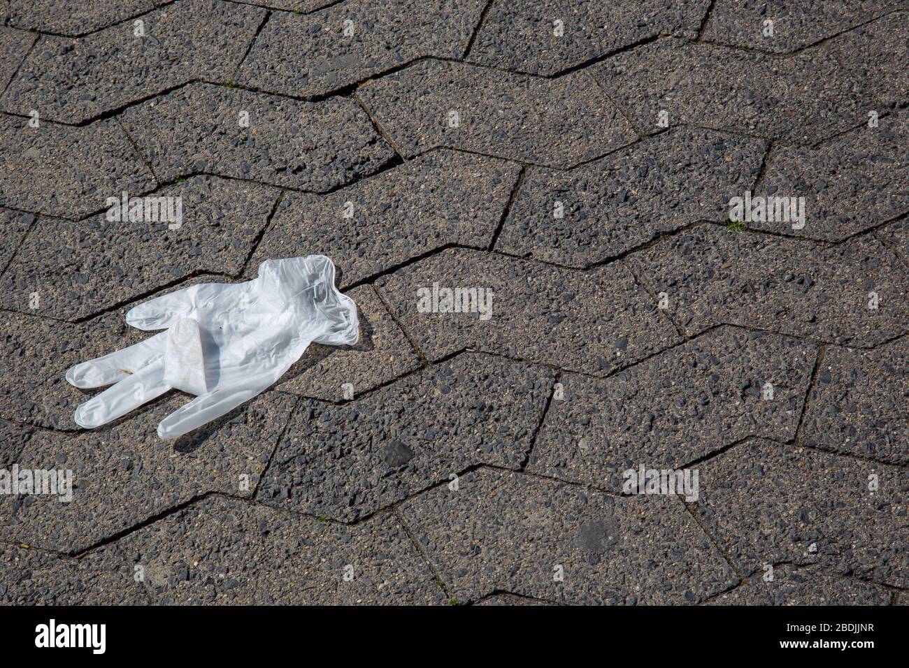 Einmalhandschuh nach der Verwendung während der Corona-Pandemie achtlos auf graue Pflastersteine entsorgt Stockfoto Einmalhandschuh nach der Verwendung während der Corona-Pandemie achtlos auf graue Pflastersteine entsorgt Stockfoto