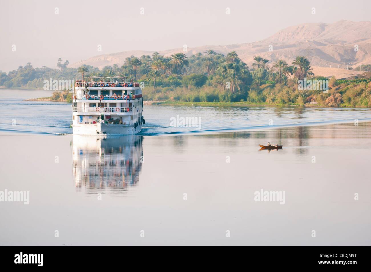 Panoramalicht auf die Boote, die auf dem Nil vorbeifahren, mit dem palmengesäumten Ufer im Hintergrund Stockfoto