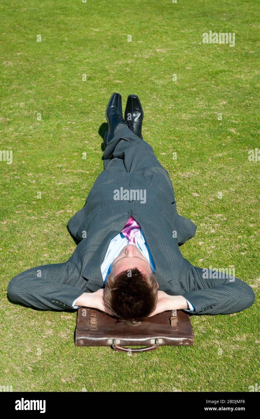 Geschäftsmann, der ein Nickerchen auf grünem Gras macht, benutzt seine Aktentasche als Kissen Stockfoto
