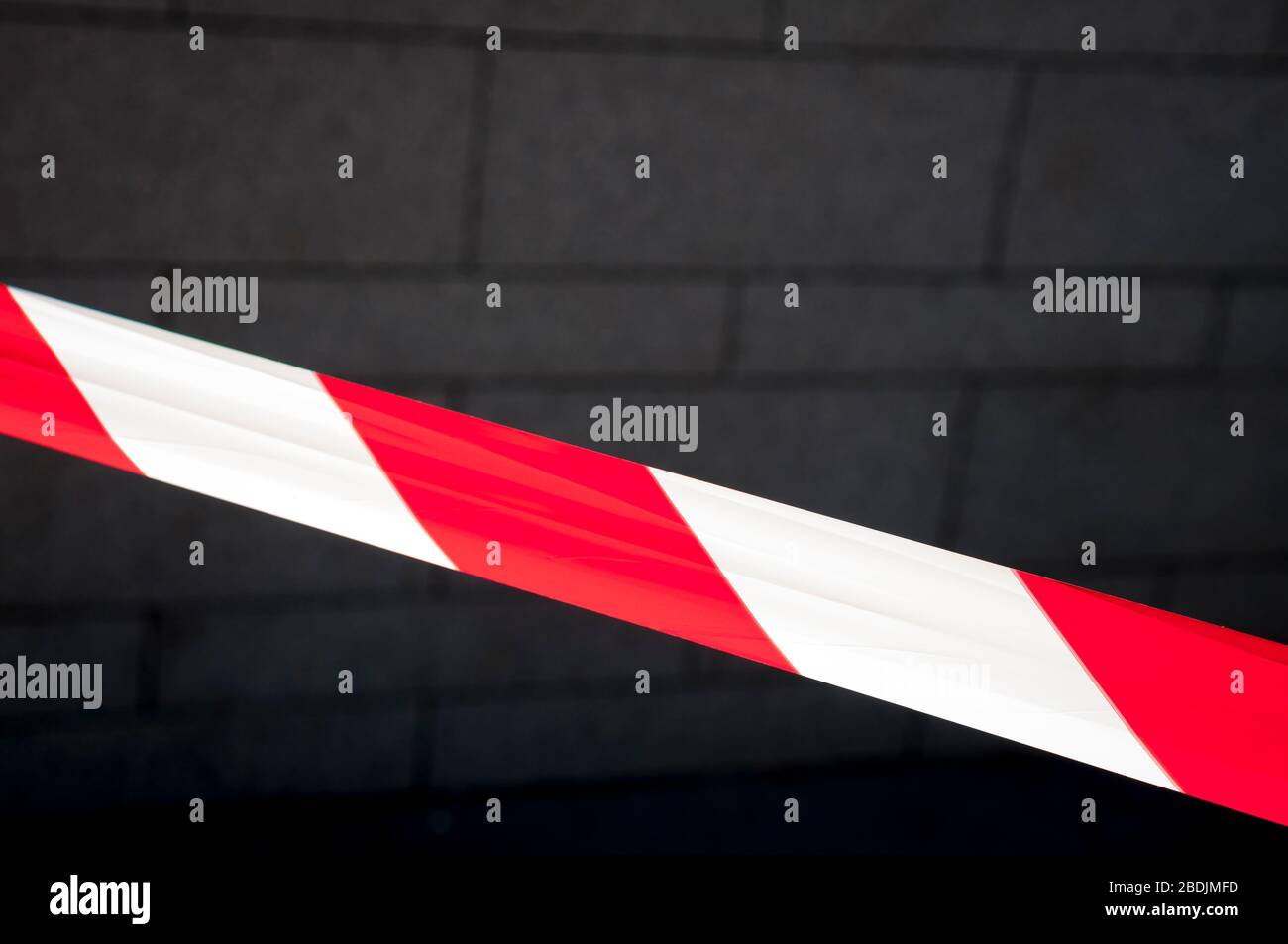 Rotes und weißes Warnband, das sich über den dunklen städtischen Backsteinwand-Hintergrund erstreckt Stockfoto
