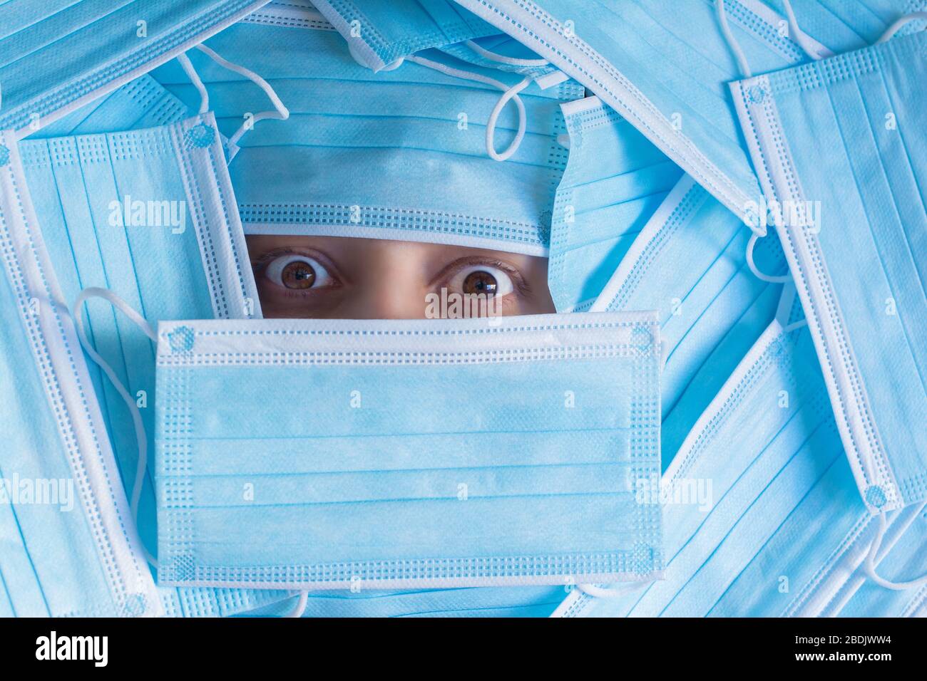 Verängstigtes Gesicht der Frau, bedeckt mit einem Haufen chirurgischer Einwegmasken. Ihre schönen Augen sind weit offen, voller empfindlicher Blutgefäße. Stockfoto