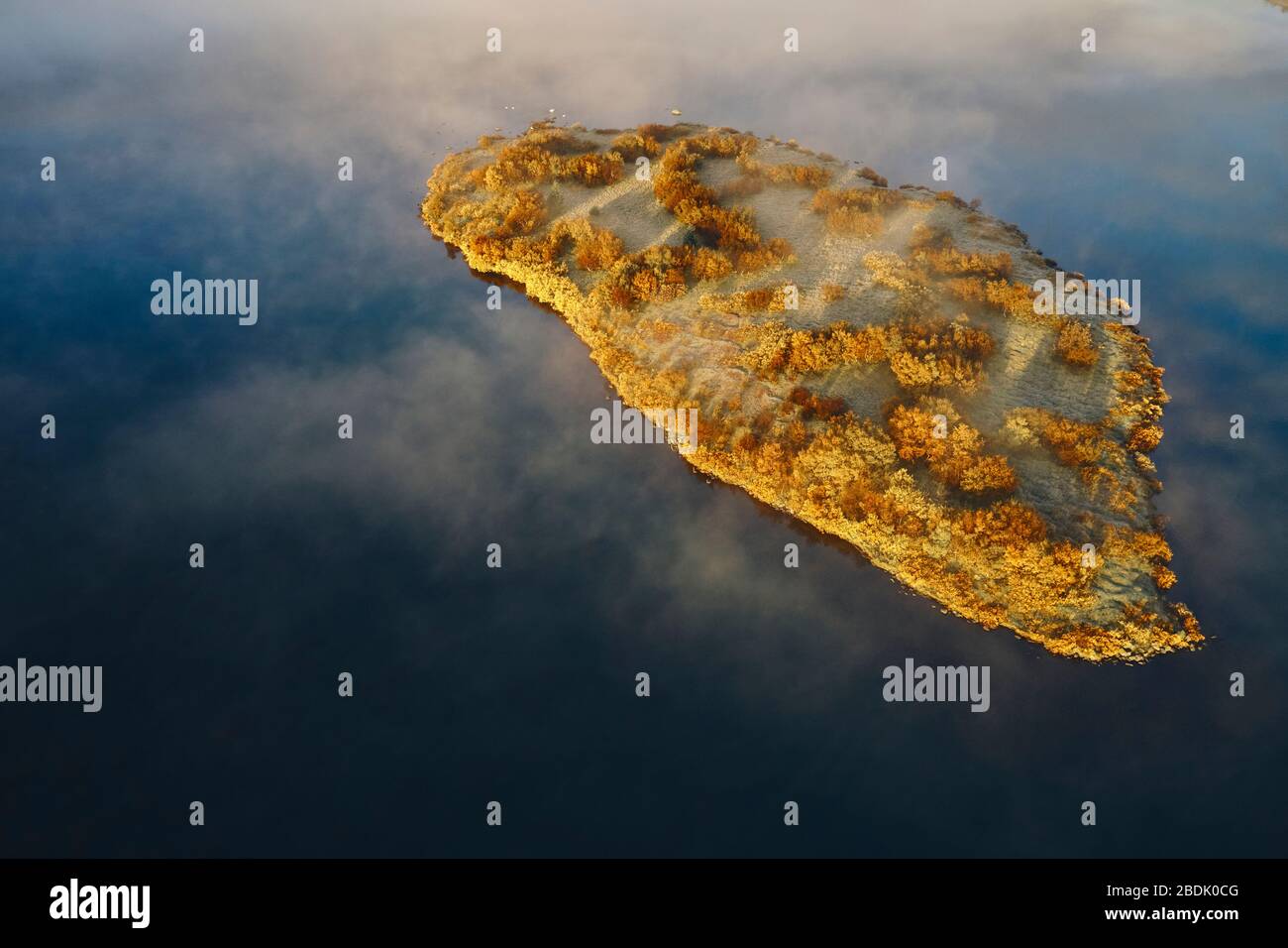 Von oben aus hat man einen Blick auf weißen Nebel, der über eine kleine Insel schwebt, mit Herbstbäumen und See mit ruhigem Wasser in der Landschaft in Island Stockfoto