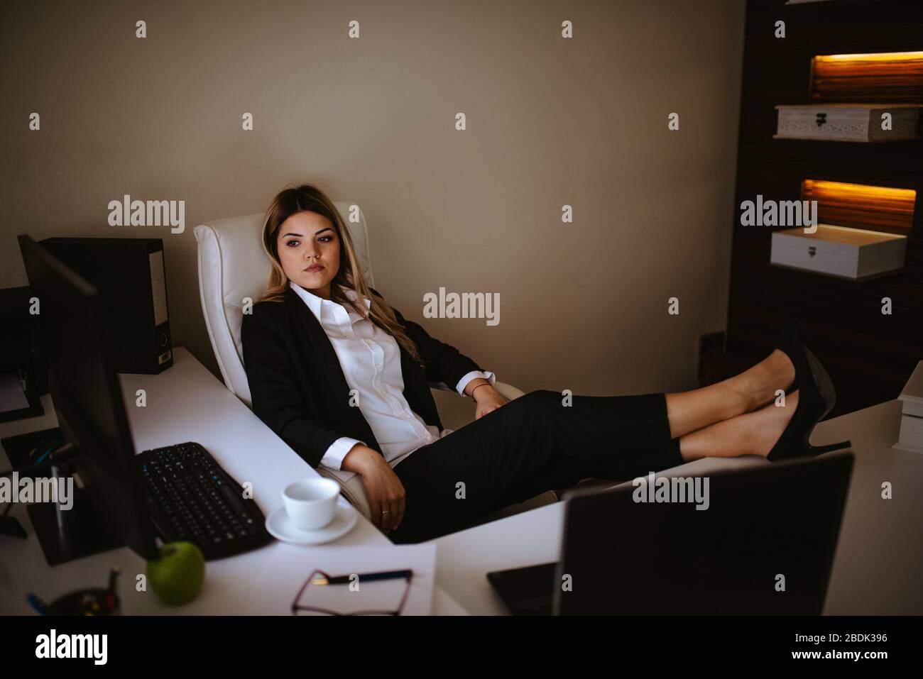 Müde junge blonde Geschäftsfrau mit den Füßen auf dem Tisch. Mode und Business Stockfoto