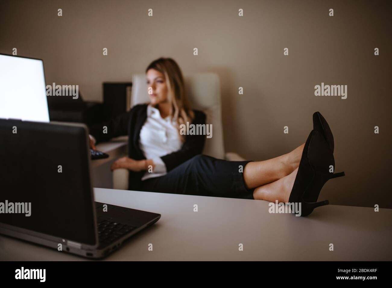 Müde junge blonde Geschäftsfrau mit den Füßen auf dem Tisch. Mode und Business Stockfoto