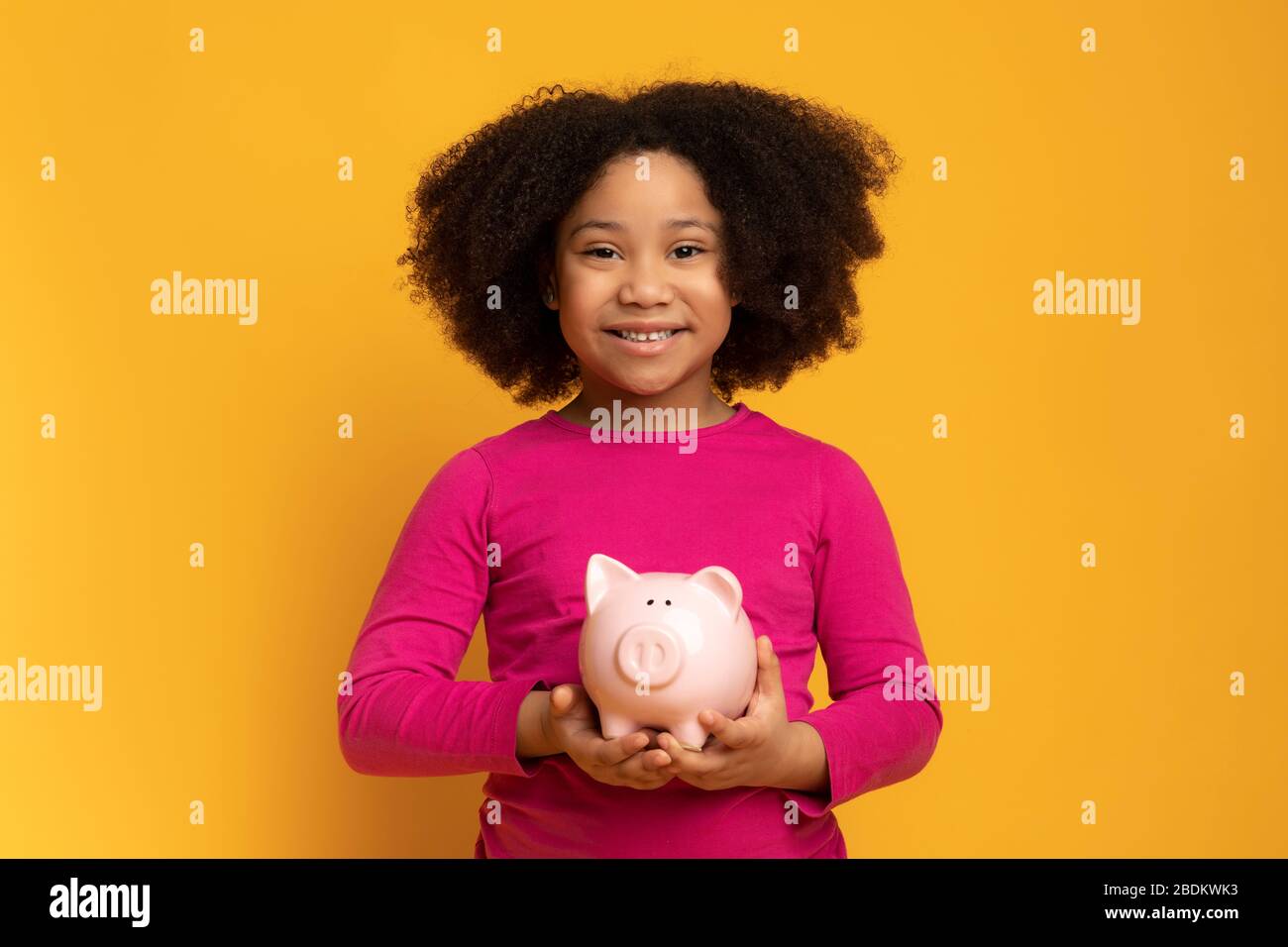 Smiling Little African American Girl Posiert Mit Piggy Bank In Den Händen Stockfoto