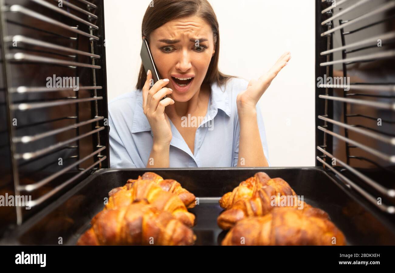 Verzweifelte Hausfrau, die um Hilfe ruft und Croissants im Ofen sucht Stockfoto