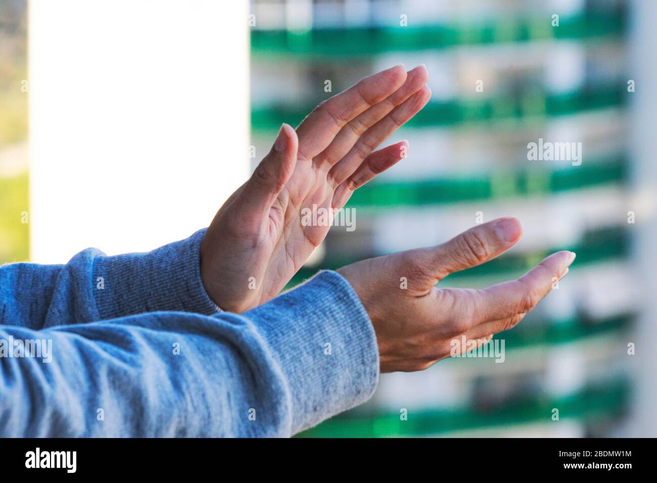 Frau übergibt sich applauderisches medizinisches Personal vom Balkon. Menschen, die sich während der Coronavirus Pandemie zur Unterstützung von Krankenschwestern, Ärzten und Krankenschwestern zusammenklatschen Stockfoto