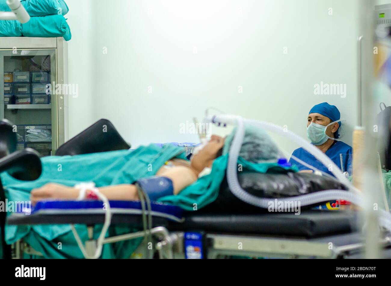 Im Operationssaal sitzt ein männlicher Operationsarzt, im Vordergrund ein Patient mit trachealer Intubation Stockfoto