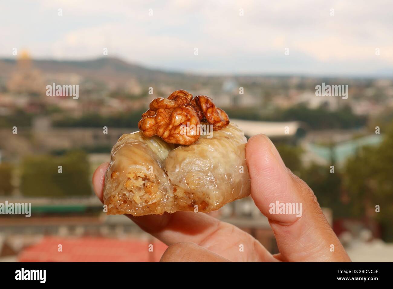 Nahaufnahme Hand Holding s Walnut Baklava Konditorei mit verschwommener City View im Hintergrund Stockfoto