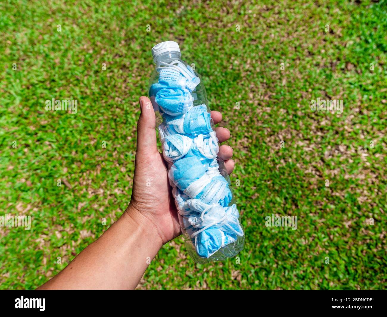 Verwendeter Maskenbegriff. Gefaltet verwendet Schutzmaske vor Littering für die Ausbreitung von Viren zu verhindern. Hand halten Flasche mit gebrauchten Maske in ihm auf gree Stockfoto