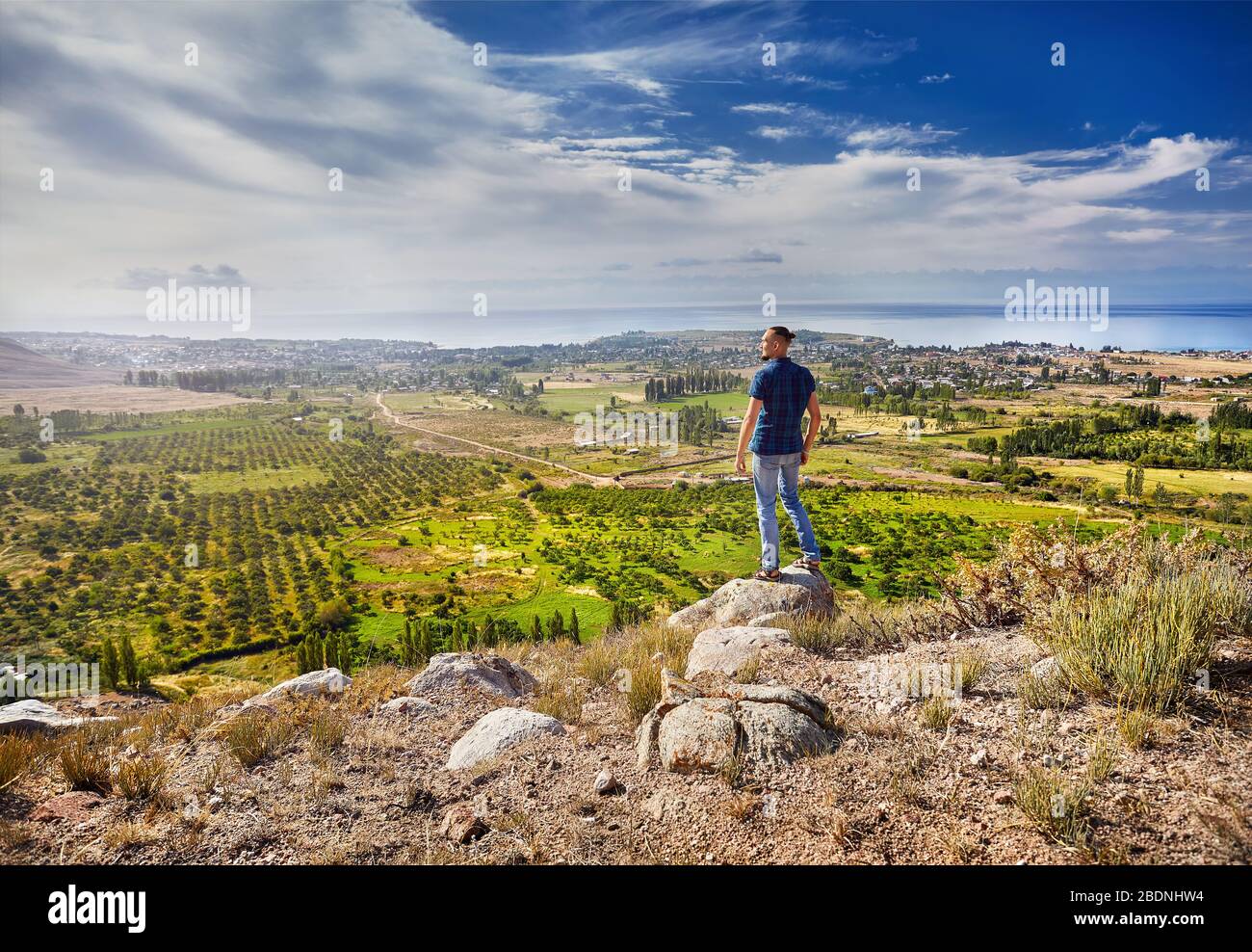 Touristische Mann in kariertes Hemd mit Blick auf die Aussicht auf das Tal mit Gärten und Dörfer in der Nähe des Issyk Kul See in Kirgisistan Stockfoto