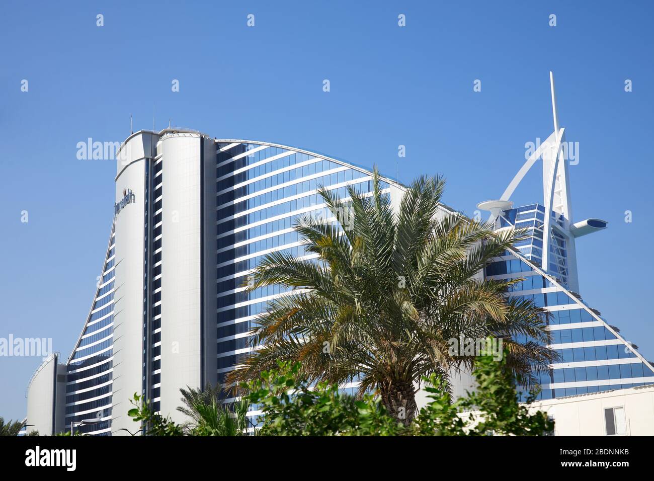 DUBAI, VEREINIGTE ARABISCHE EMIRATE - 22. NOVEMBER 2019: Jumeirah Beach und Burj Al Arab Luxury Hotel mit Palme an einem sonnigen Tag, blauer Himmel in Dubai Stockfoto