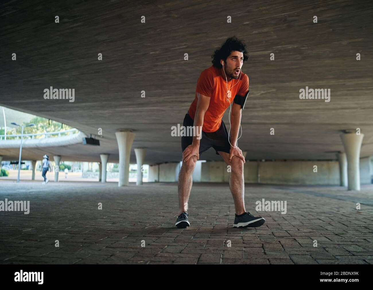Attraktiver sportlicher junger Mann in Runner-Sportbekleidung atmet nach dem Laufen unter der Brücke und macht eine Pause - Mann läuft im neuen Stockfoto