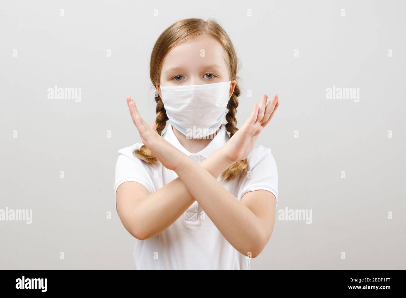 Ein kleines Mädchen in einer schützenden medizinischen Maske zeigt eine Stopp-Geste mit den Händen während einer Coronavirus-Pandemie. Porträt eines Kindes auf grauem Hintergrund Stockfoto