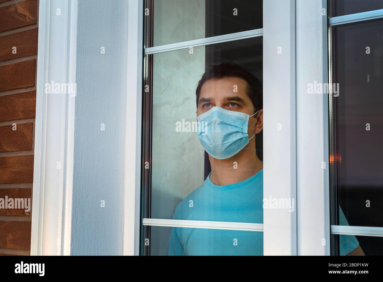 Mann mit einer schützenden medizinischen Maske am Fenster. Stockfoto