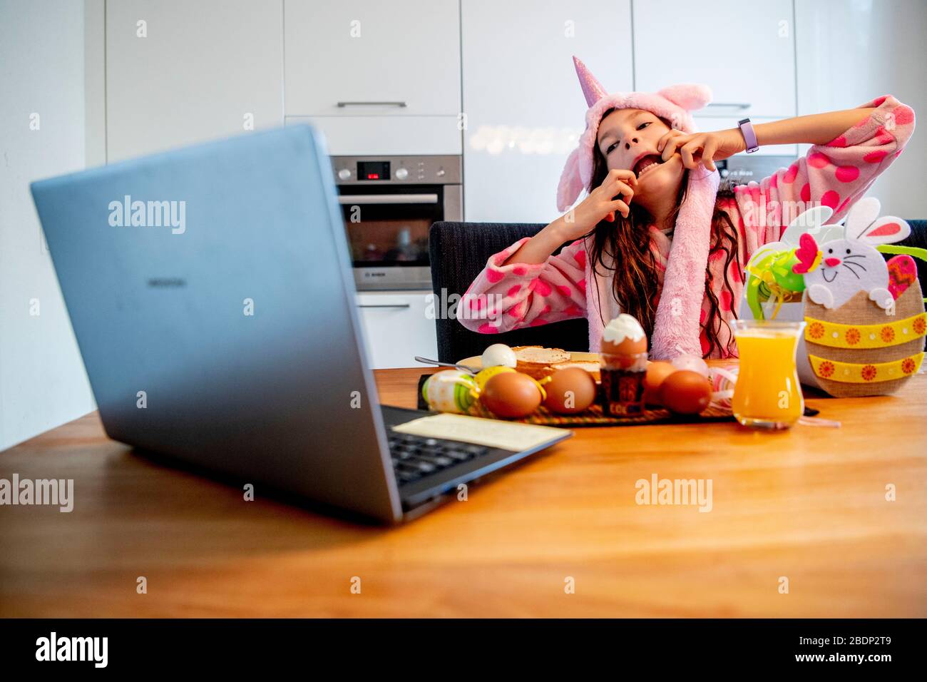 Ein 9-jähriges Mädchen, das ihr digitales Osterfrühstück mit ihrer Klassenkameradin auf ihrem Laptop hat, während sie Online-Video-Kommunikationsdienste von zu Hause aus unter Androhung von Coronavirus nutzt. Stockfoto