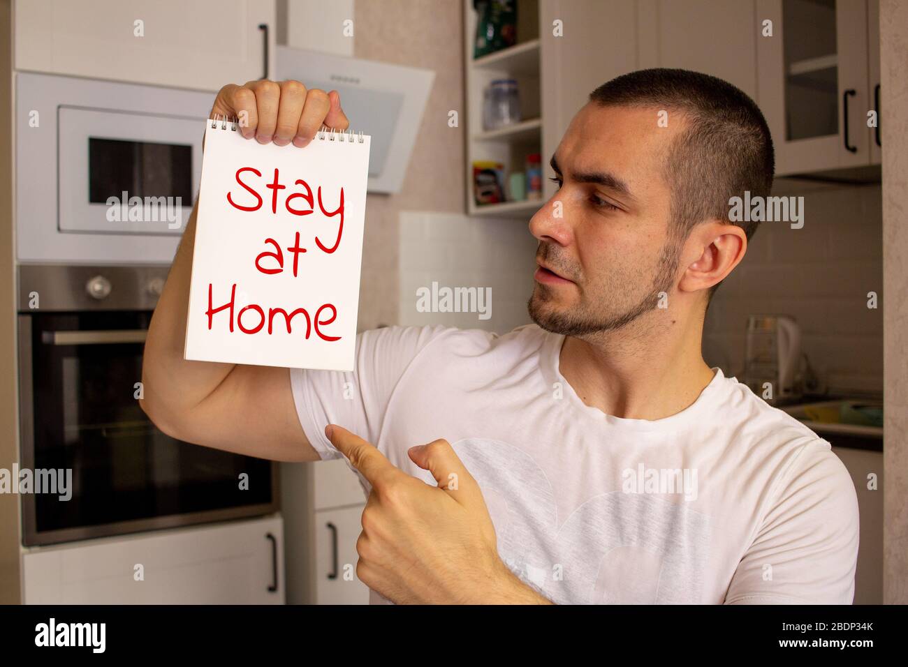 Während der COVID-19-Sperre bleibt ein junger Mann ohne Maske zu Hause. Halten Papier zu Hause bleiben Text. Stockfoto