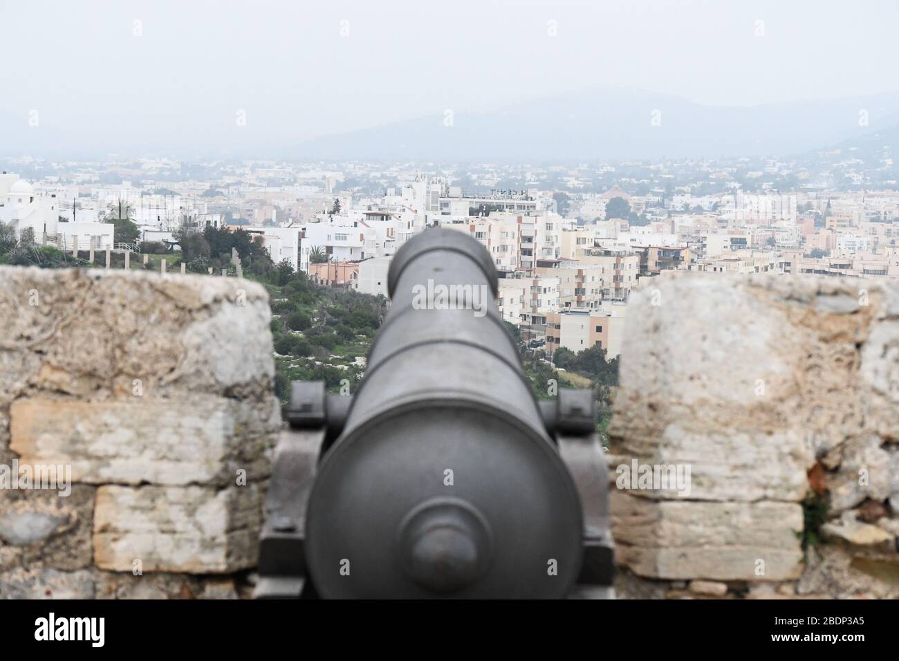 Schwarze Kriegskanone, die von einem alten Schloss auf ibiza auf eine Stadt zeigt Stockfoto