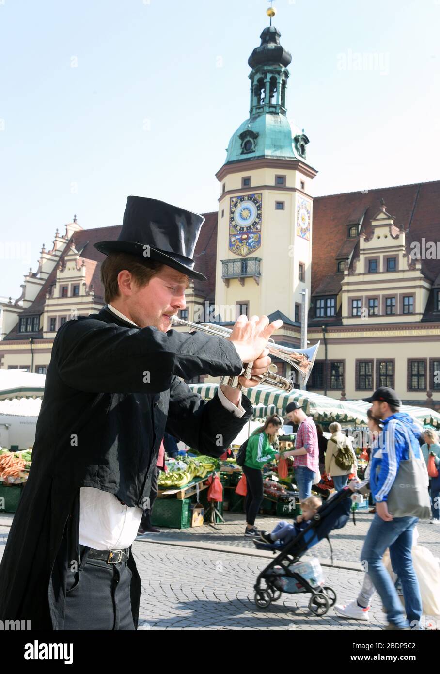 Leipzig, Deutschland. April 2020. Ein Londoner Straßenmusiker spielt seine Serenaden in Schwänzen und Kopfhut für die Händler auf dem Wochenmarkt und die Besucher. Der Leipziger Wochenmarkt findet mit deutlich verlängerten Abständen zwischen den einzelnen Ständen statt. Die Landesbehörden in Sachsen überprüfen auch, ob die Fernverkehrsregeln auf den Wochenmärkten während der Corona-Krise eingehalten werden. Nachdem die Volksmärkte zunächst verboten waren, sind sie seit dem 1. April wieder zugelassen. An den Ständen müssen die Besucher aber eine Distanz von zwei Metern halten. Credit: Dpa Picture Alliance / Alamy Live Stockfoto