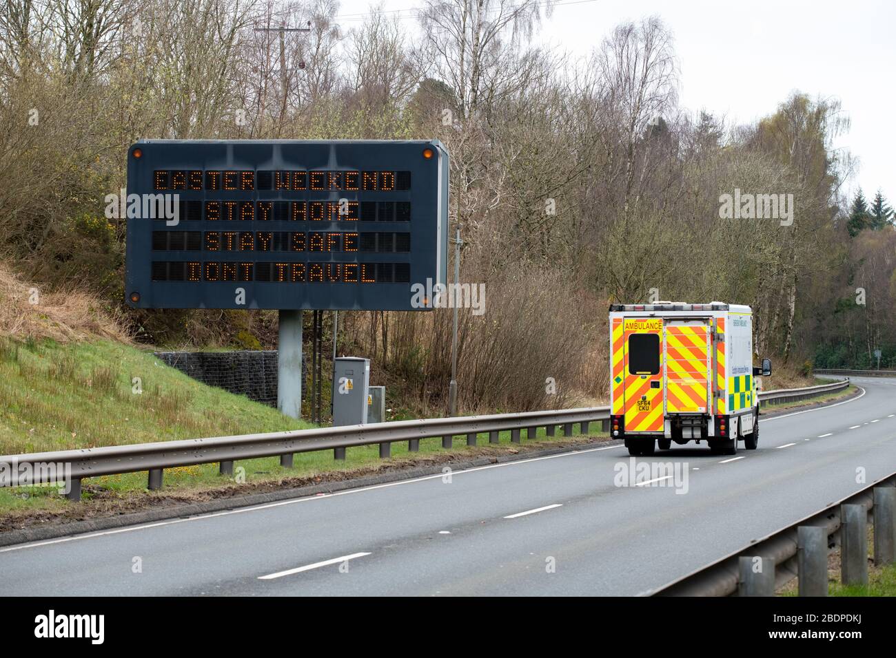 A82 von Loch Lomond, Schottland, Großbritannien. April 2020. Reisesorgen am Osterwochenende - ein Krankenwagen passiert ein Schild, in dem die Menschen aufgefordert werden, zu Hause zu bleiben und nicht über das osterwochenende auf der A82 nordwärts an der Seite von Loch Lomond Credit zu reisen: Kay Roxby/Alamy Live News Stockfoto